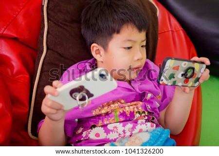 Asian Chinese boy playing smartphone on bed. watching smartphone. kid use phone and play game. child use mobile. addicted game and cartoon
