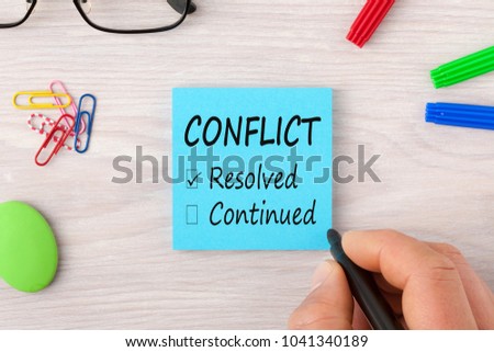 Hand writing Conflict, Resolved and Continued on note with marker pen and glasses on wooden desk. Business Concept. Top view. Royalty-Free Stock Photo #1041340189