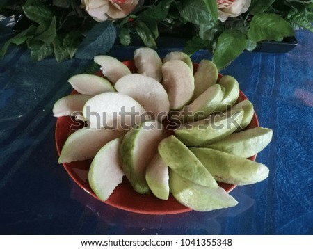 Slices of guava fruit arranged on a plate Brown. On the table is a blue cloth and a bouquet of roses placed behind.