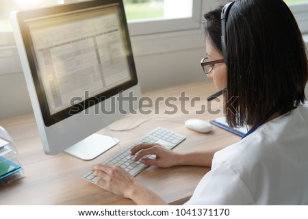 Medical secretary typing report on deskop computer Royalty-Free Stock Photo #1041371170