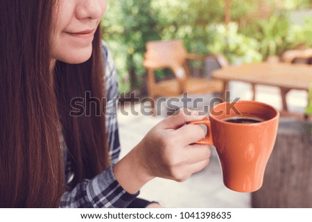 Closeup image of an Asian woman holding and drinking hot coffee with feeling good in the garden
