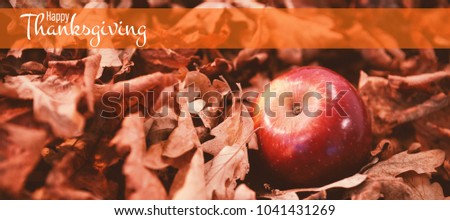 Illustration of happy thanksgiving day text greeting against autumn leaves with apple