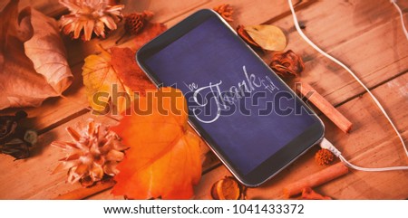 Digital image of happy thanksgiving day text greeting against mobile phone on wood table surround of leaf