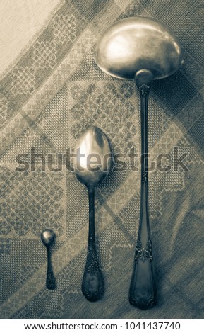 On linen tablecloth silverware, old spoons of different sizes. Household, female responsibilities, kitchen. Muted tone, vignetting.
