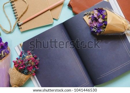 The notebook is placed on a blue background and is decorated with a bouquet of dried flowers, making it beautiful and attractive, with a space on the paper for use.

