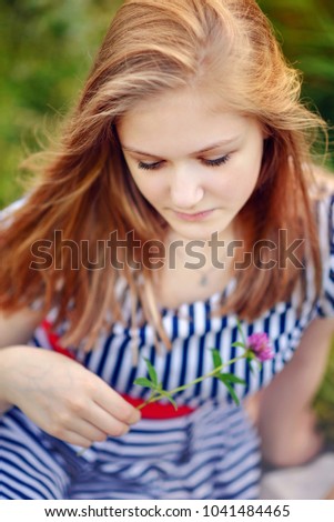 Teenage girl with a flower sitting on the grass in the summertime park