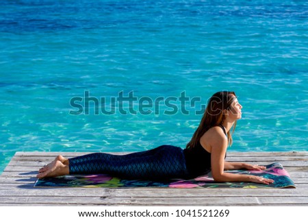Young latin woman practicing yoga on the beach, doing Ardha bhudjangasana, baby Cobra pose. Outdoors Yoga. Cancun. Riviera Maya.