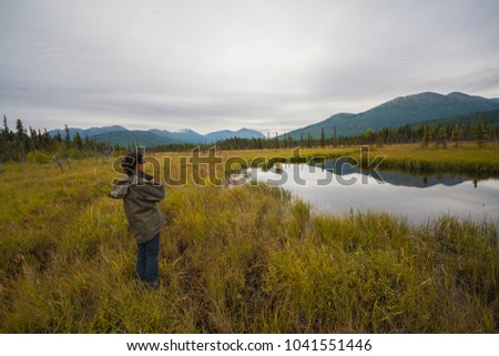 Alaskan landscape with lake in the picture.  Boreal vegetation with clouds in bad weather. Young girl watching lake in Alaska.