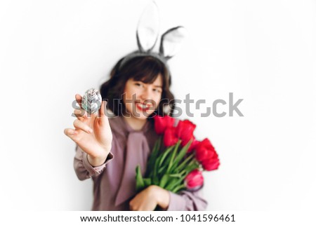 happy Easter. beautiful stylish girl in bunny ears and pink tulips holding easter egg on white background isolated. easter hunt concept. happy woman holding painted egg. seasons greetings