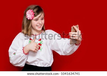 A cute little girl in bows hold telephone and take picture on red background. Communication concept