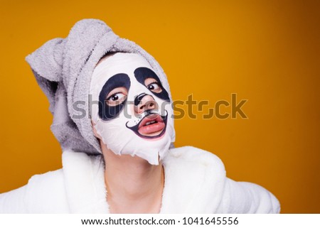 a dazed woman with a towel on her head apply a moisturizing mask on her face, in the form of a muzzle of a panda