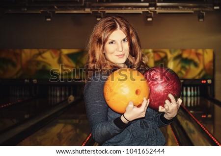 Beautiful girl is holding a bowling ball, looking at camera and smiling ready to play bowling