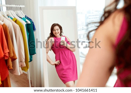 clothing, fashion and people concept - happy plus size woman in pink dress taking at mirror selfie by smartphone at home