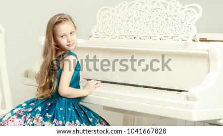 Caucasian little girl with long blond hair, in a beautiful pink skirt and white T-shirt and a pink bow on her chest.She plays music with the piano.