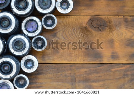 Several photographic lenses lie on a brown wooden background. Space for text