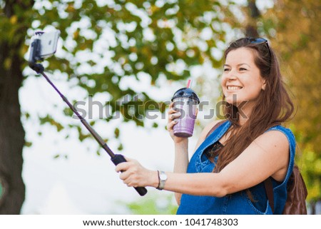 Young woman with smoothie selfie stick photo herself outdoors. trendy girl have fun with her smartphone shooting for video blog or social net