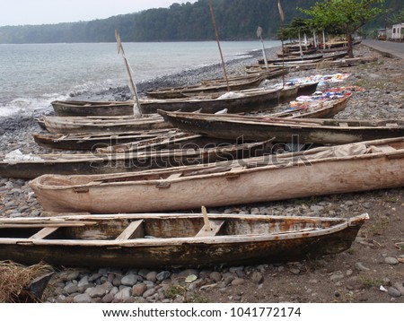 Outdoor scene with many small wooden boats on the beach. Picture taken in a coastal village of sao tome island in africa. Traditional pirogues aligned on a rocky beach with the sea in background.  