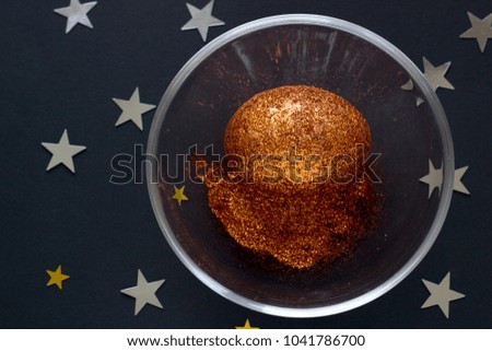 Brilliant egg in glass bowl on dark background with shine lights stars. Top view concept with bronze egg in flat lay style. Idea for greetings and Easter.
