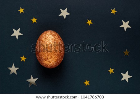 Brilliant egg with copy space for text on dark background with shine lights stars. Top view concept with bronze egg in flat lay style. Idea for greetings and Easter.
