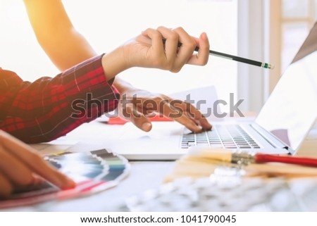 Young asian decorator using laptop with house project,looking color swatches,painting roller and paint brushes,teamwork,idea,construction concept.	