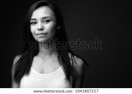 Studio shot of young Asian woman against gray background in black and white