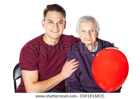 Picture of a smiling grandmother and her cheerful grandson embracing and holding a red balloon