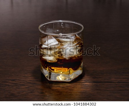 A glass of whiskey and ice on the table.