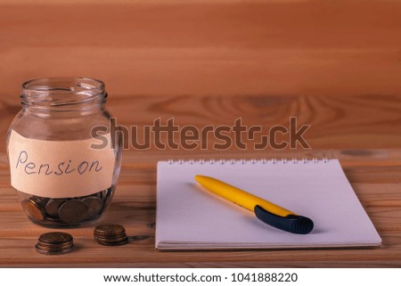 glass jar with pension inscription with coins inside and outside, notebook with pen in close-up