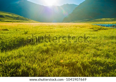 sun is coming up from over the hill, lighting up an lake down in valley.Grass,rocks and mountains also featured in the picture.green field, mountains and cloudy sky sunset. Beautiful landscape, grass