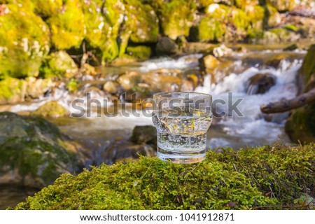 Pure water in clear glass on green moss background with river in background, diet and fitness background