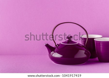 Purple teapot and cups on a lilac background with copy space.