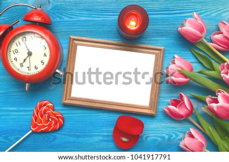 Tulip flowers wedding ring in a gift present box and empty photo frame of a loved one copy space on blue wooden table board background. Marriage offer. Woman day concept. Saint Valentines day.