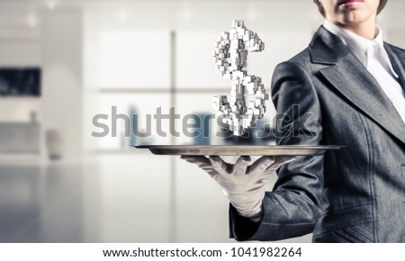 Cropped image of waitress's hand in white glove presenting multiple cubes in form of dollar sign on metal tray with office view on background.