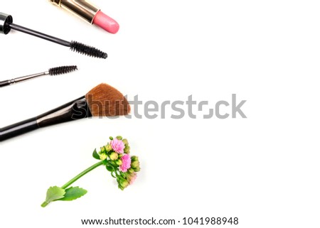 Makeup brush, mascara applicator, lipstick, and a flower, shot from above on a white background with copy space. A template for a makeup artist's business card or flyer design