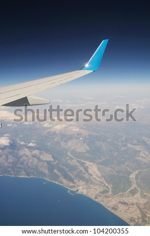 Airplane's wing under mountains and sea