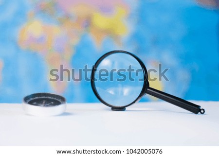 Compass and magnifier on the background of the geographical map - the theme of travel