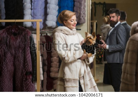 Woman in white fur coat with dog and bearded macho looking for new overcoat. Girl with cunning face wearing white mink fur. Couple shopping concept. Couple in love shops in fur mall.