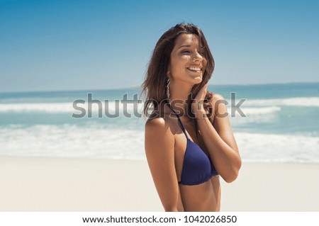 Portrait of young woman in blue bikini walking on tropical beach. Beautiful girl relaxing and enjoying vacation at sea. Smiling woman enjoying and thinking at seaside with copy space.