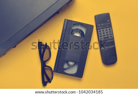 Vhs player, video cassette, 3d glasses, tv remote on a yellow background. Obsolete media technologies. Top view.
