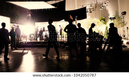 Behind the scenes or the making of film video production and movie crew team working in silhouette of camera and equipment set in studio.  Royalty-Free Stock Photo #1042050787