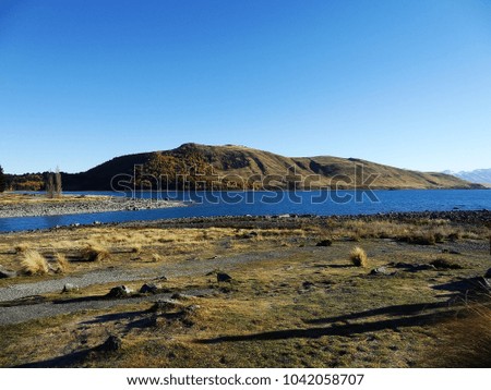Beautiful scenery with hills, bushes, blue sky & blue waters at Lake Tekapo, New Zealand, South Island