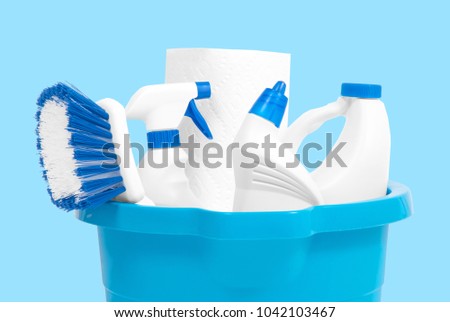 Variety of cleaning products in bucket on pastel blue background