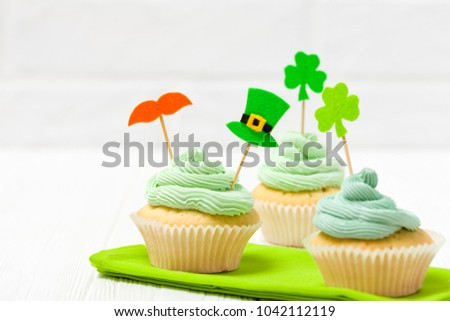 St. Patrick's Day theme colorful horizontal banner. Cupcakes decorated with green buttercream and craft felt decorations in form of leprechaun hat and mustache and shamrock leaves on white background.