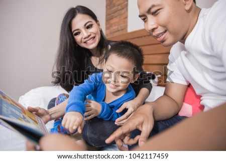 Kid boy and his father reading a book in bed accompanied by mom