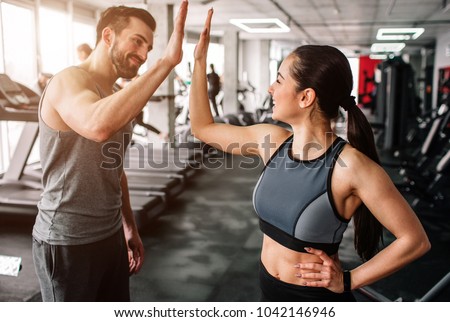 A beautiful girl and her well-built boyfriend are greeting each other with a high-five. They are happy to see each othr in the gym. Young people are ready to start their workout. Royalty-Free Stock Photo #1042146946