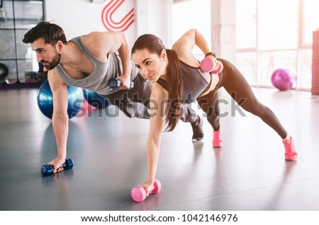 Good picture of boy and girl standing on the carpet with the dumbells in one hand and putting another hand with a dumbell behind the back