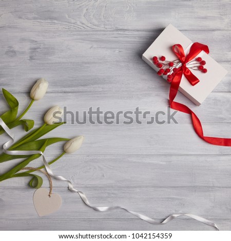 Stylish craft present box and greeting card and white tulips on white wooden rustic background. Holiday gift. Top view with copy space