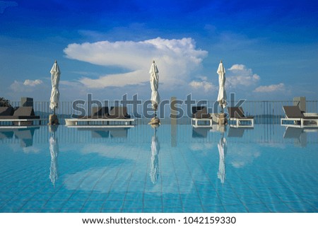 Swimming pool with blue water, beach bed, and sea under summer sky.
