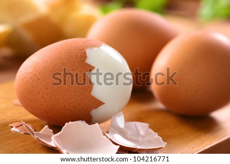 Fresh hard boiled eggs with shell beside on wooden board (Selective Focus, Focus on the front of the shell on the first egg) Royalty-Free Stock Photo #104216771