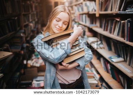 Nice and warm picture of attractive girl hugging books that she holds in her hands. She has closed her eyes and put her head over the books. Young woman looks happy.